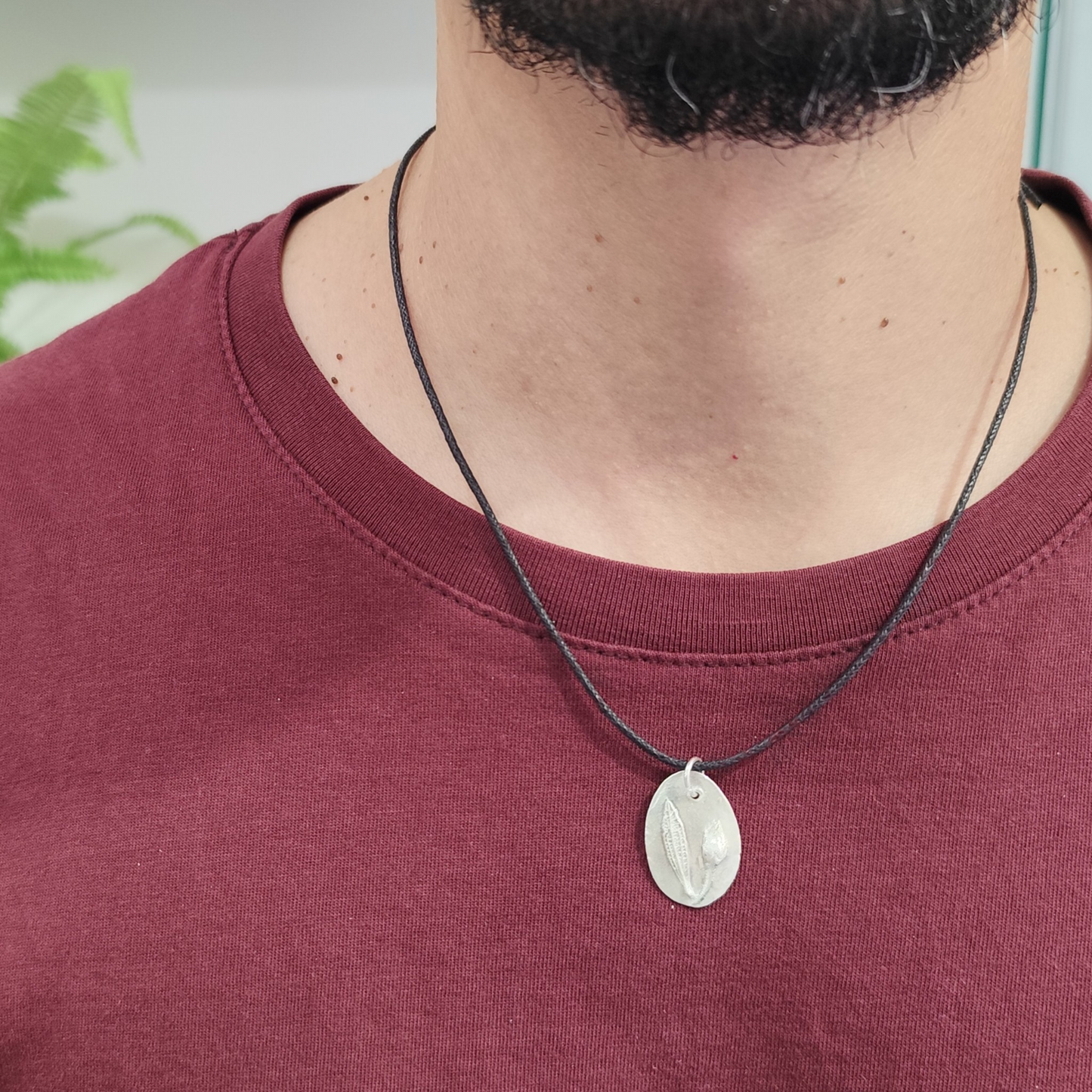 Hombre con medalla de plata con capullo y hoja de jara en relieve y cordón negro de algodón