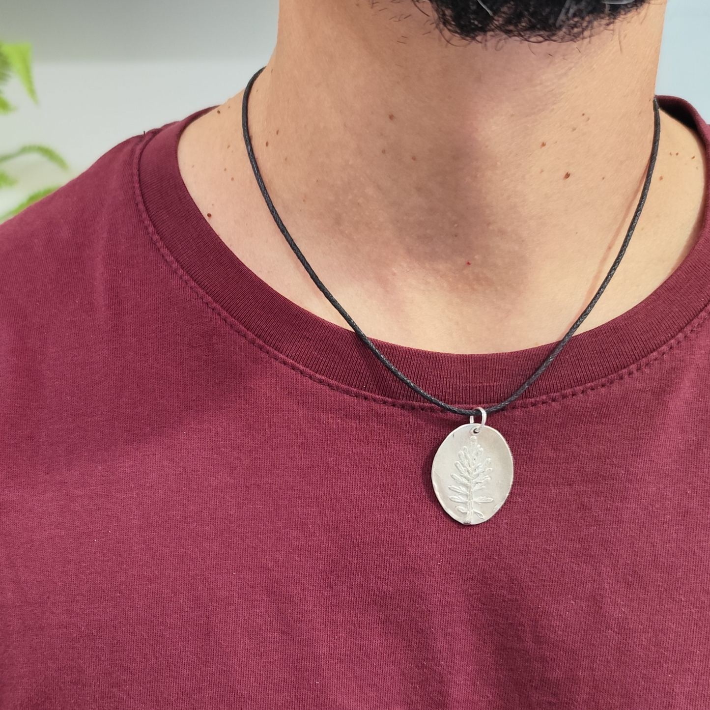 Hombre con medalla de plata con hoja de coronas de reina en relieve y cordón negro de algodón
