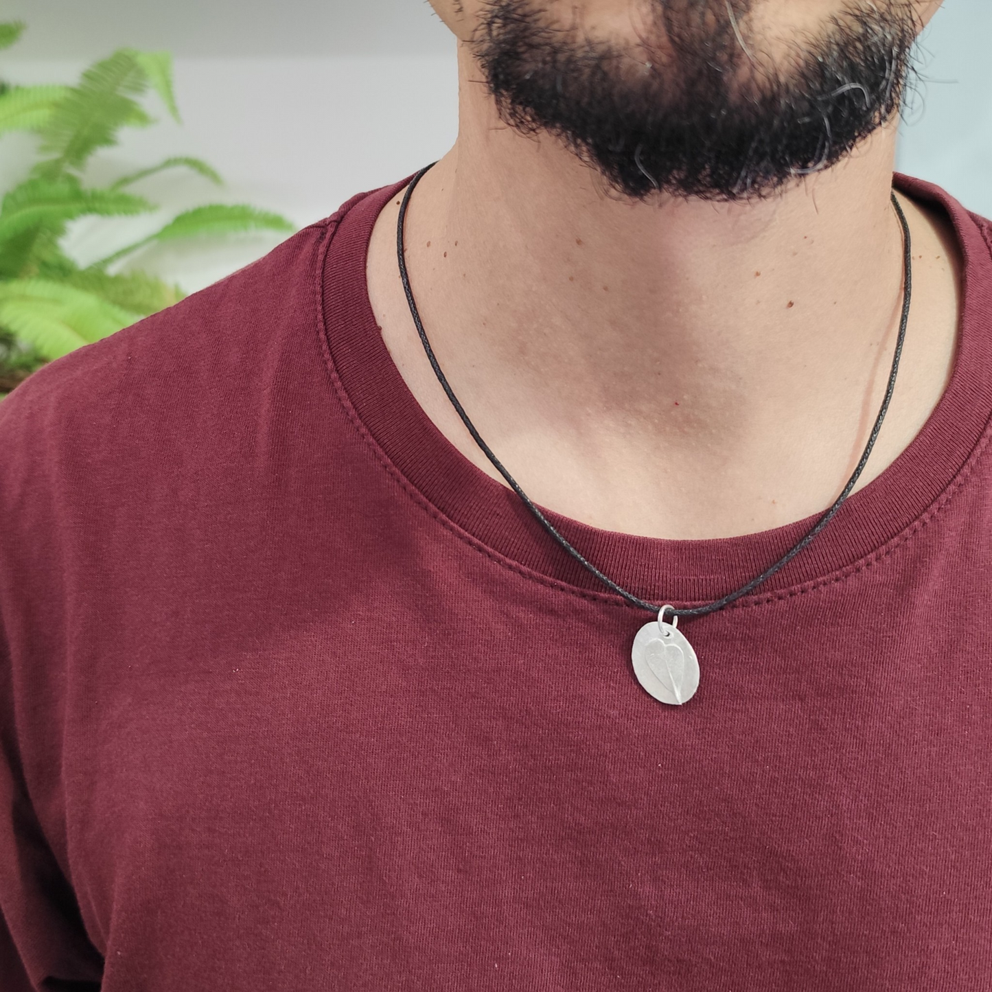 Hombre con medalla de plata con huella de hoja de haya romana en relieve y cordón negro de algodón