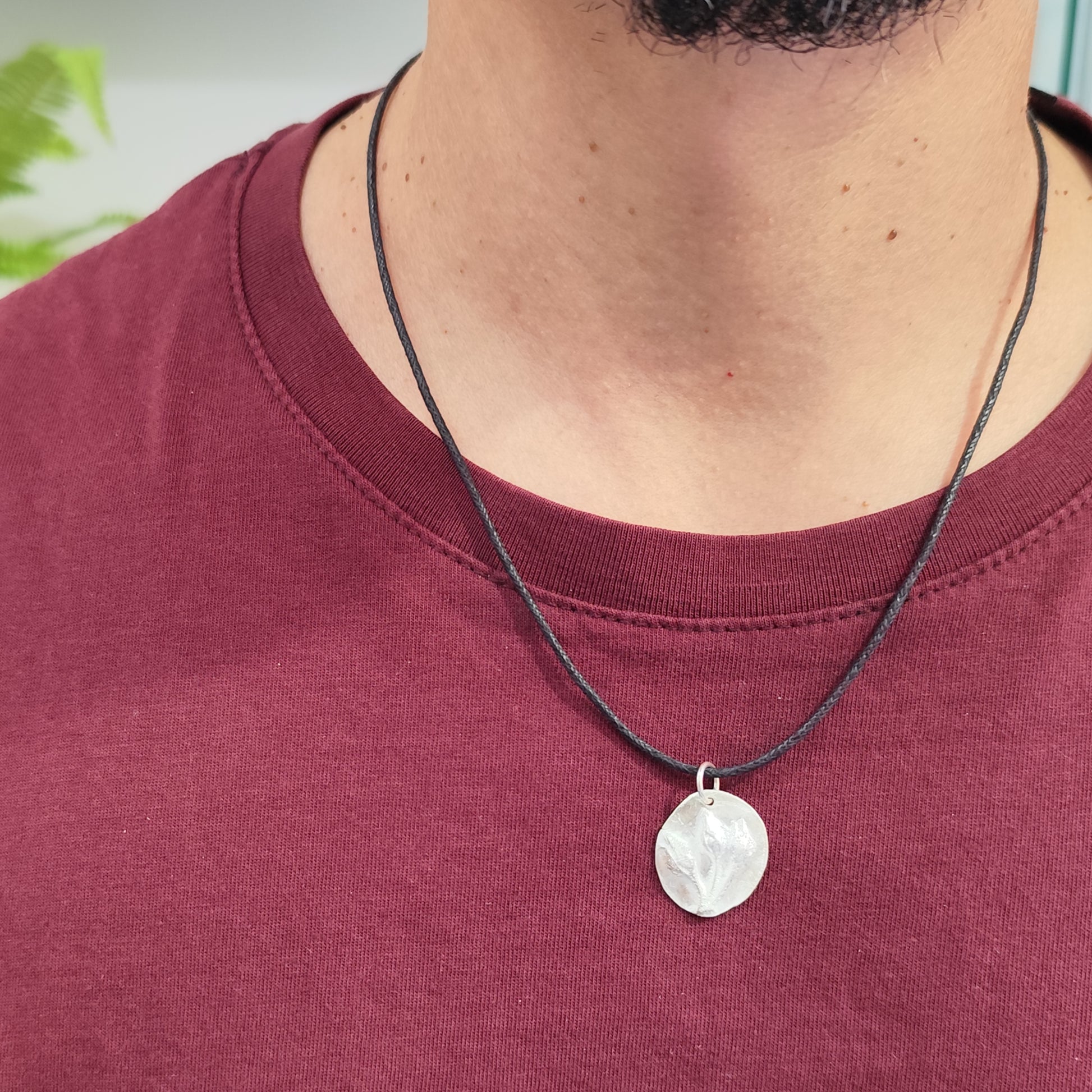 Hombre con medalla de plata con capullos de jara en relieve y cordón negro de algodón