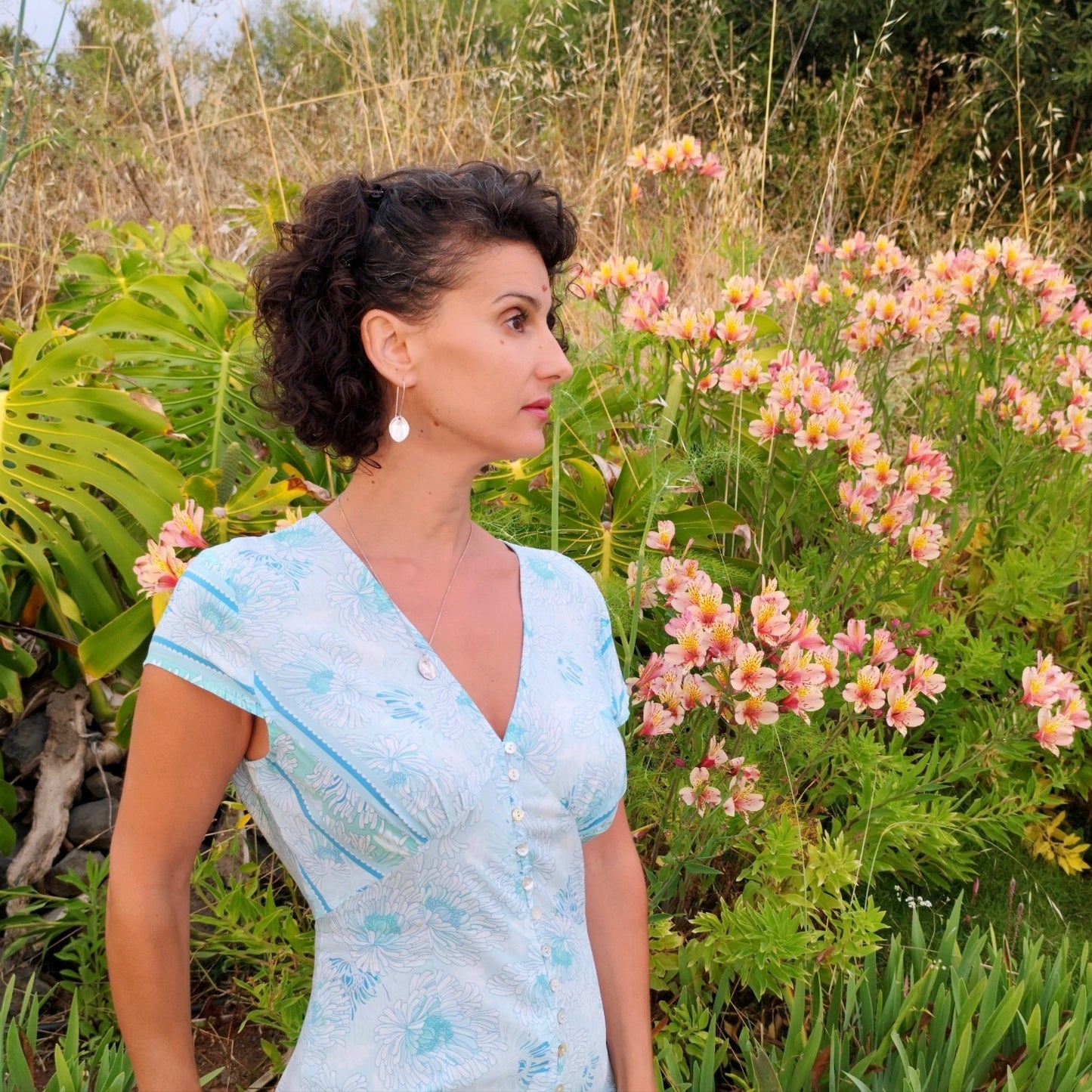 Mujer de perfil con Vestido Acuarela largo estampado en tonos turquesa y verde, con fondo de plantas y flores en Canarias.