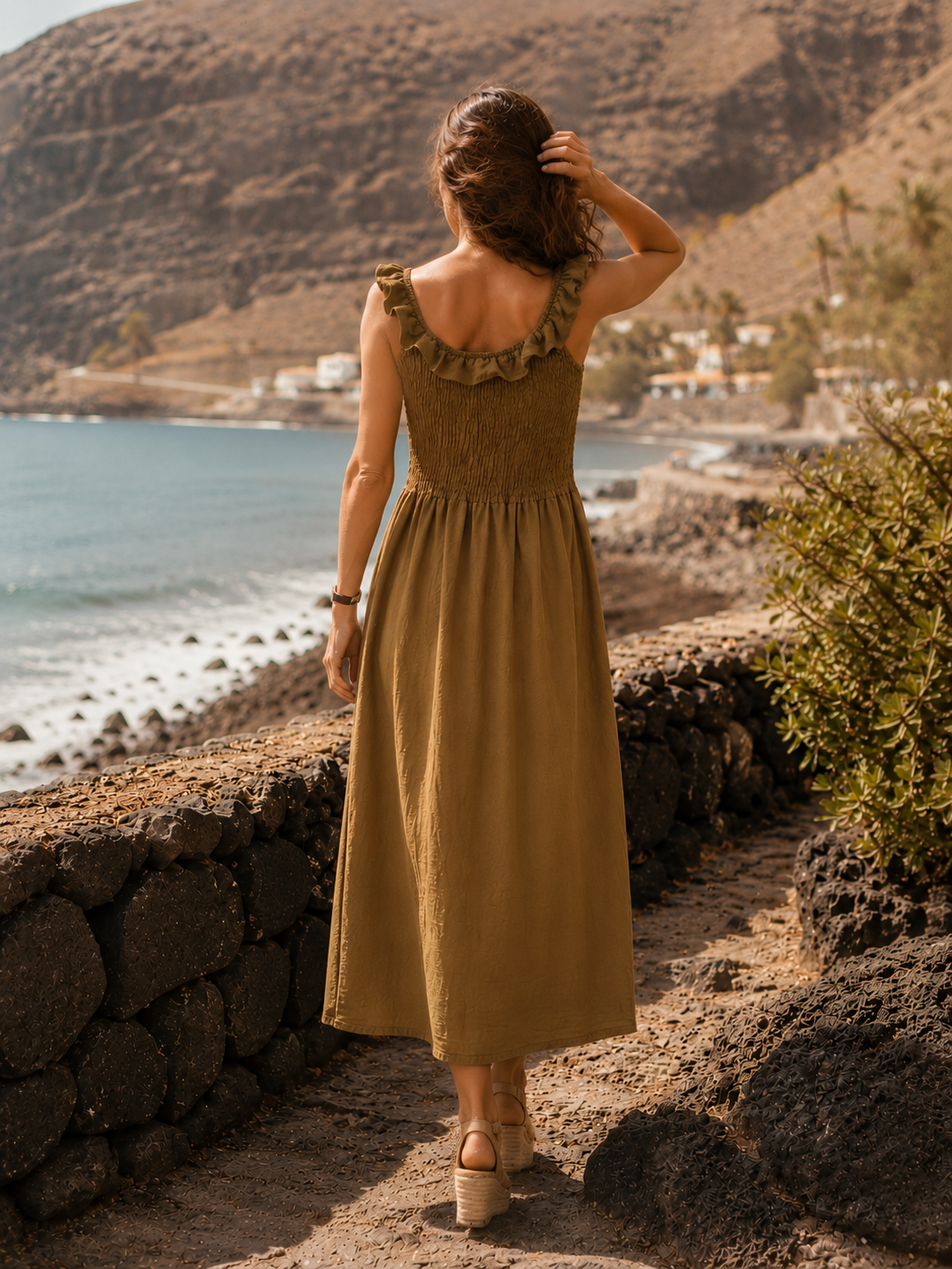 Vestido Retama de la colección Esencia visto de espaldas, con cuerpo de nido de abeja y volante, frente al paisaje costero