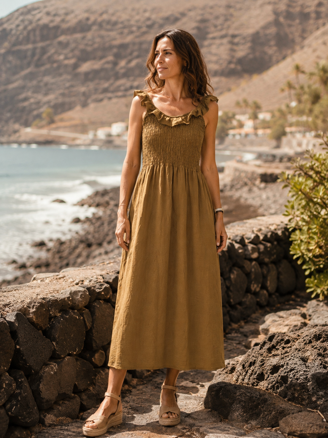 Vestido Retama de la colección Esencia en tono verde oliva, modelo de frente con paisaje costero de La Gomera