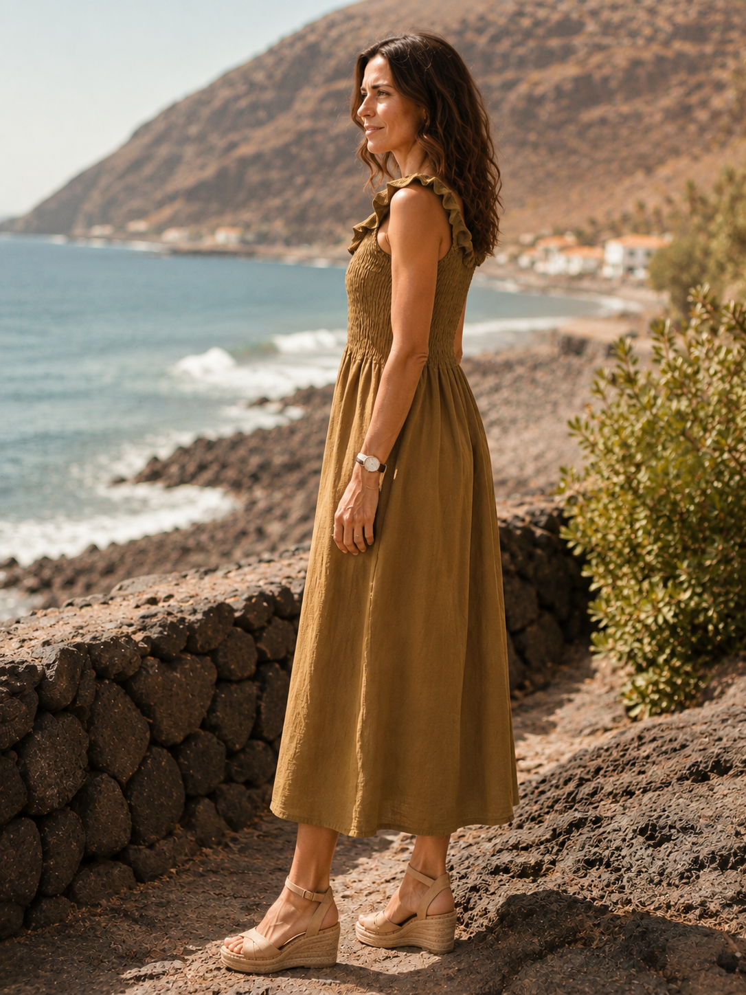 Vestido Retama de la colección Esencia visto de perfil, con caída fluida y paisaje costero de fondo